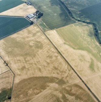 Oblique aerial view centred on the cropmarks of the pit-defined cursus, pits and rig, with farmhouse, pits, rig, ring-ditch and possible quarry adjacent, taken from the WNW.