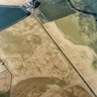 Oblique aerial view centred on the cropmarks of the pit-defined cursus, pits and rig, with farmhouse, pits, rig, ring-ditch and possible quarry adjacent, taken from the NW.