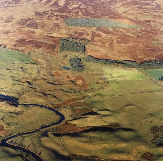 Oblique aerial view centred on the remains of farmsteads, buildings, hut circles, small cairns, banks, huts and rig, taken from the SW.