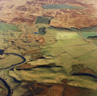 Oblique aerial view centred on the remains of farmsteads, buildings, hut circles, small cairns, banks, huts and rig, taken from the SSW.
