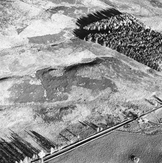 Oblique aerial view centred on the remains of buildings with hut circles, small cairns, banks, and huts adjacent, taken from the W.