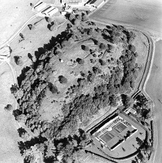 Oblique aerial view centred on the remains of the vitrified fort and broch with the house, walled garden and lodge adjacent, taken from the SW.