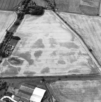 Oblique aerial view centred on the cropmarks of the pits, ringditches, field drain and possible enclosure, with the farmstead, chapel and burial-ground adjacent, taken from the SE.