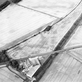 Oblique aerial view centred on the cropmarks of the enclosure, pits, rig and ring-ditch, with the farmhouse and farmsteading adjacent, taken from the SW.