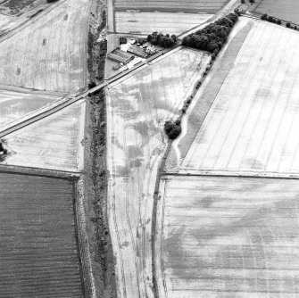 Oblique aerial view centred on the cropmarks of the enclosure, pits, rig and ring-ditches, with the farmhouse and farmsteading adjacent, taken from the ENE.