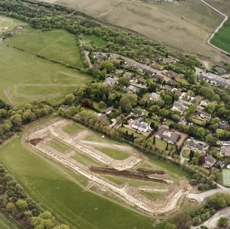 Oblique aerial view centred on the excavations at Dullatur Roman Camps with the Antonine Wall nearby, taken from the SE