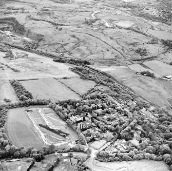 Oblique aerial view centred on the excavations at Dullatur Roman Camps with the Antonine Wall nearby, taken from the E