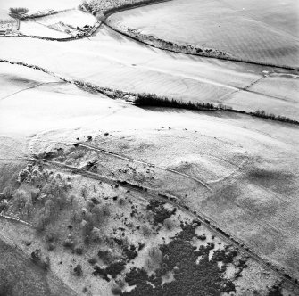 Oblique aerial view centred on the remains of the fort, settlement and cairn, taken from the NE.