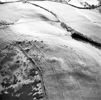 Oblique aerial view centred on the remains of the fort, settlement and cairn, taken from the N.