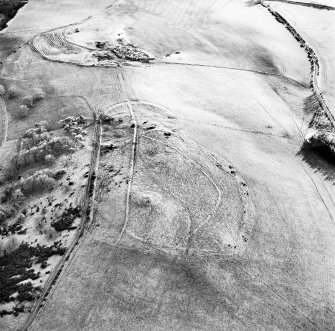 Oblique aerial view centred on the remains of the fort, settlement and cairn, taken from the NNW.