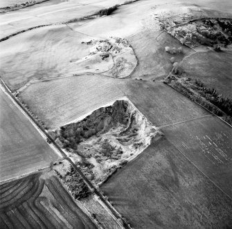 Oblique aerial view centred on the remains of the quarry with fort, settlement and cairn adjacent, taken from the ESE.