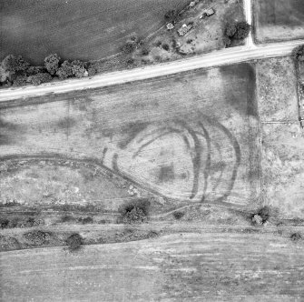 Oblique aerial view centred on the sequence of defensive ditches, revealed as cropmarks, around the fort at Wester Carmuirs. Within the fort there are traces of a roundhouse.The cropmarks of a palisaded enclosure (NS88SW 50), also containing a roundhouse, are also visible on the photograph.