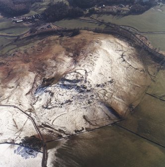 Oblique aerial view centred on the remains of the fort, settlements and field system with the farmsteading adjacent, taken from the NNE.