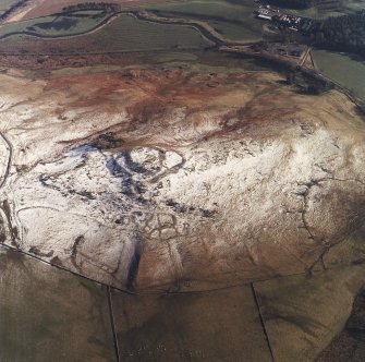 Oblique aerial view centred on the remains of the fort, settlements and field system with the farmsteading adjacent, taken from the NW.