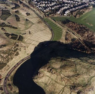 Oblique aerial view of Holyrood Park centred on the remains of a fort, field bank and scooped settlement, taken from the SW.