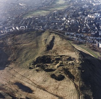 Oblique aerial view of Holyrood Park centred on the remains of quarries with a fort and bank adjacent, taken from the ENE.