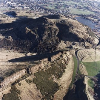 Oblique aerial view of Holyrood Park centred on the remains of quarries on Salisbury Crags with Arthur's Seat behind, taken from the WSW.