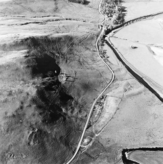 Oblique aerial view centred on the remains of the tower-house, buildings and enclosures with the inn and field adjacent, taken from the S.