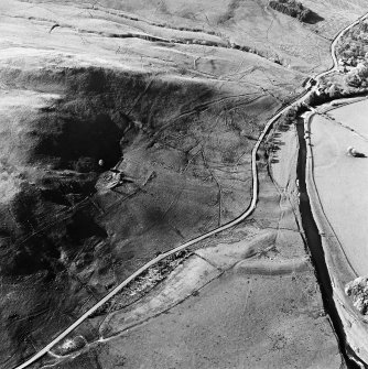 Oblique aerial view centred on the remains of the tower-house, buildings and enclosures with the inn and field adjacent, taken from the SSE.