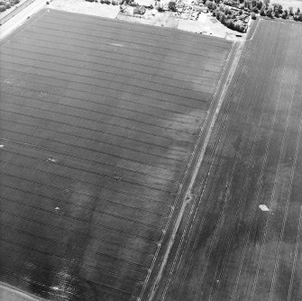 Oblique aerial view centred on the cropmarks of the ring-ditch and possible unenclosed settlement with other cropmarks including those of the palisaded enclosure, rig and enclosure, adjacent, taken from the NNE.