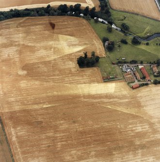Oblique aerial view centred on the burial-ground, watermill, farmhouse, farmsteading and school, and the cropmarks of the nunnery, taken from the NNW.