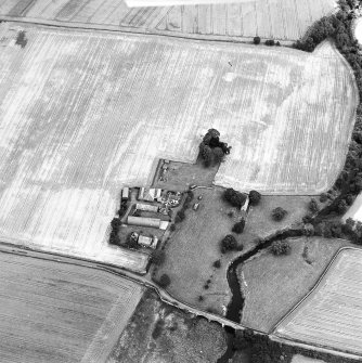 Oblique aerial view centred on the burial-ground, watermill, farmhouse, farmsteading and school, and the cropmarks of the nunnery, taken from the SW.