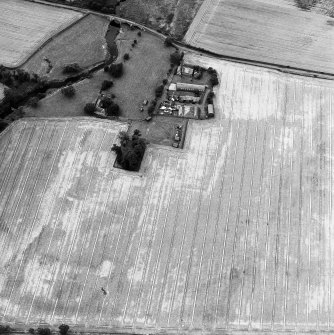 Oblique aerial view centred on the burial-ground, watermill, farmhouse, farmsteading and school, and the cropmarks of the nunnery, taken from the NE.