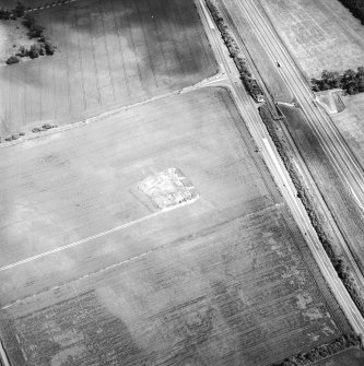 Oblique aerial view centred on the excavation of the settlement with the standing stone adjacent, taken from the W.