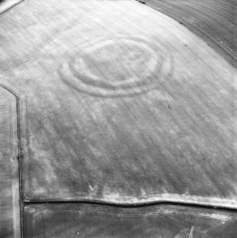 Oblique aerial view centred on the cropmarks of the fort with field boundaries and  cropmarks adjacent, taken from the SSE.