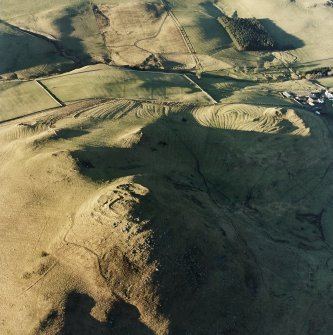 Oblique aerial view centred on the remains of the fort with rig, enclosures and cairn adjacent, taken from the SE.