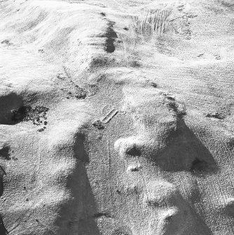 Oblique aerial view centred on the remains of the building and enclosures with rig adjacent, taken from the ENE.