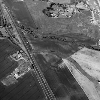 Thorntonloch, oblique aerial view, taken from the SSW, centred on the cropmarks of a fort and an enclosure, and showing a Smithy in the top right-hand corner of the photograph.