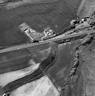 Thorntonloch, oblique aerial view, taken from the NE, centred on the cropmarks of a fort and an enclosure, and showing the cropmark of a possible ring-ditch in the top centre of the photograph.