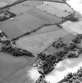 Oblique aerial view centred on the cropmarks of the possible enclosures and linear cropmarks with the church, burial ground, manse, country house, lodge, school, farmhouses, farmsteadings and cottages adjacent, taken from the NE.