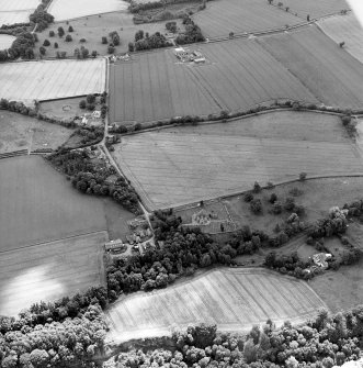 Oblique aerial view centred on the cropmarks of the possible enclosures and linear cropmarks with the church, burial ground, manse, country house, lodge, school, farmhouses, farmsteadings and cottages adjacent, taken from the NNE.