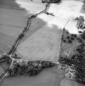 Oblique aerial view centred on the possible enclosures and linear cropmarks with the church, burial ground, lodge, school, farmhouses, farmsteadings and cottages adjacent, taken from the ENE.