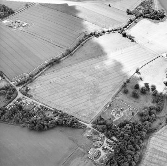 Oblique aerial view centred on the possible enclosures and linear cropmarks with the church, burial ground, lodge, school, farmhouses, farmsteadings and cottages adjacent, taken from the ENE.