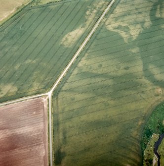 Oblique aerial view centred on the cropmarks of the enclosure and unenclosed settlement with the cropmarks of the rig adjacent, taken from the ENE.