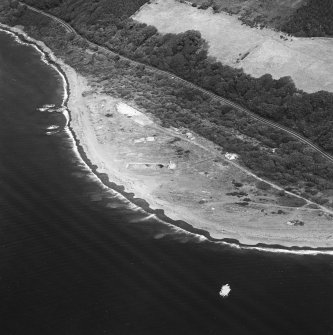 Oblique aerial view centred on the remains of the pile construction yard, scuttled ships, railway yard and railway, taken from the SW.