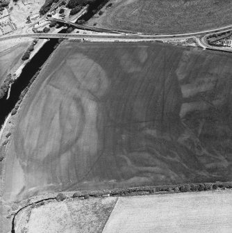 Ballantrae Bridge, oblique aerial view, taken from the SW, centred on the cropmarks of field boundaries and areas with pits. A souterrain and a round house are visible in the top right-hand corner of the photograph, and Ballantrae Bridge is shown in the top left-hand corner.