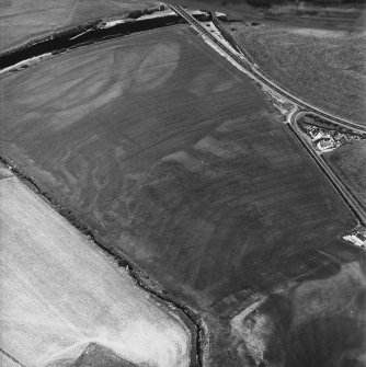 Ballantrae Bridge, oblique aerial view, taken from the S, centred on the cropmarks of a barrow and four poster stone-circle, and on an area with pits, field boundaries and linear cropmarks. Two possible souterrains, possible enclosures and various other cropmarks are also visible in the photograph.