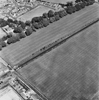 Dunragit, oblique aerial view, taken from the SE, centred on an area defined as a cropmark complex. Cropmarks of a roman road and quarry pits are visible in the top right-hand corner of the photograph.