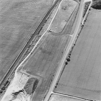 Oblique aerial photograph of Drumflower taken from the E, centred on the cropmarks of barrows, pits and a pit-alignment with the line of a military road to the N.