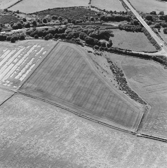 Oblique aerial photograph of Glenluce taken from the E, centred on the cropmarks of a Roman temporary camp.