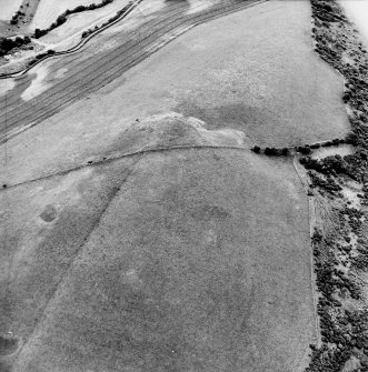 Oblique aerial view centred on the parchmarks of the palisaded settlement with quarries and field boundaries adjacent, taken from the NE.