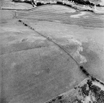 Oblique aerial view centred on the parchmarks of the palisaded settlement with quarries and field boundaries adjacent, taken from the N.