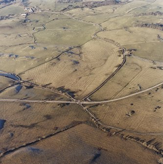 Oblique aerial view centred on the remains of rig with church, burial ground, homestead moat and building adjacent, taken from the SE.