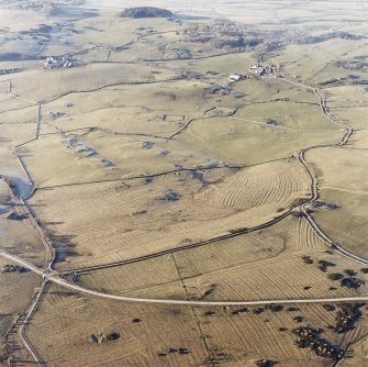 Oblique aerial view centred on the remains of rig with church, burial ground, homestead moat and building adjacent, taken from the ESE.