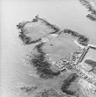 Oblique aerial view centred on the remains of the chapel with the remains of the promontory fort and the village adjacent, taken from the N.