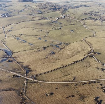 Oblique aerial view centred on the remains of rig with church, burial ground, homestead moat and building adjacent, taken from the ESE.